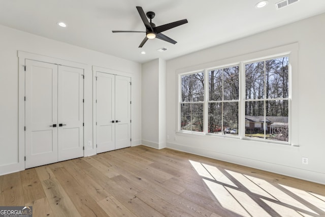 unfurnished bedroom with light wood-type flooring, visible vents, recessed lighting, and two closets