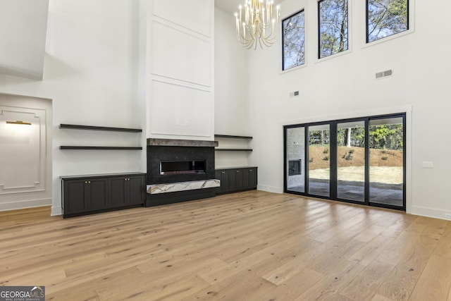 unfurnished living room with visible vents, a premium fireplace, a chandelier, light wood-type flooring, and baseboards