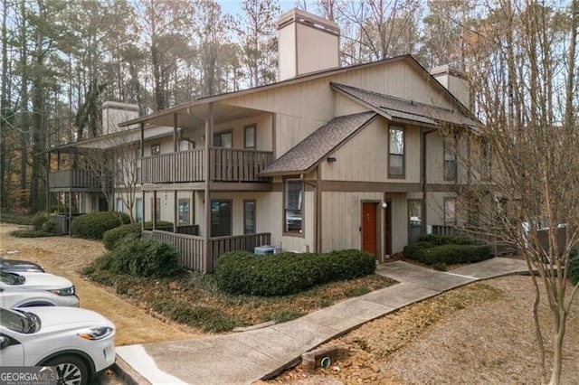 view of front of home featuring a shingled roof, a chimney, and a balcony