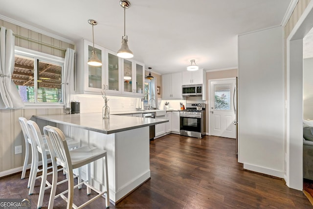 kitchen with stainless steel appliances, a peninsula, white cabinets, ornamental molding, and glass insert cabinets