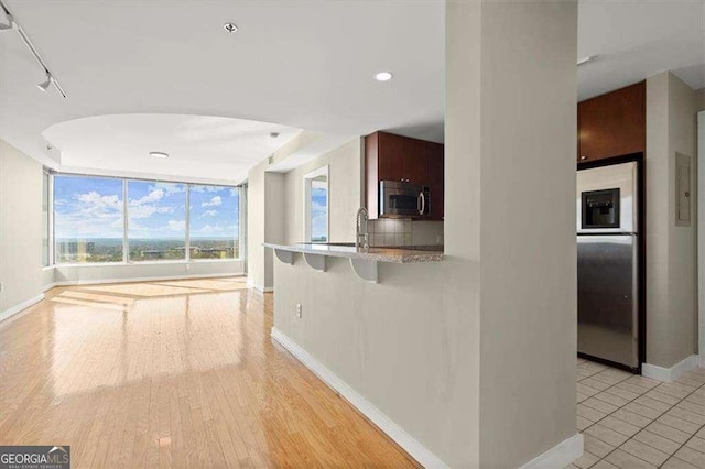 kitchen with baseboards, light wood-style flooring, appliances with stainless steel finishes, a kitchen breakfast bar, and a sink