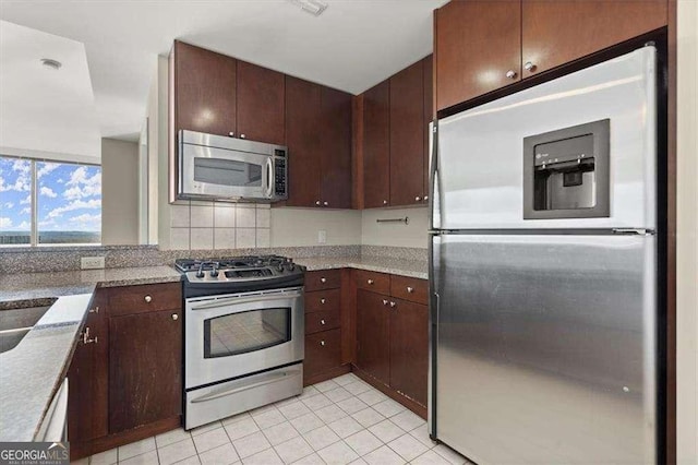 kitchen featuring light tile patterned floors, light stone counters, stainless steel appliances, and dark brown cabinets