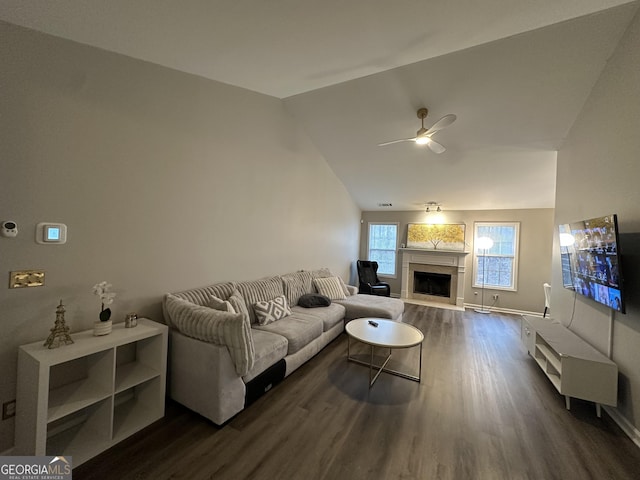 living area featuring a fireplace with raised hearth, a ceiling fan, baseboards, vaulted ceiling, and dark wood-style floors