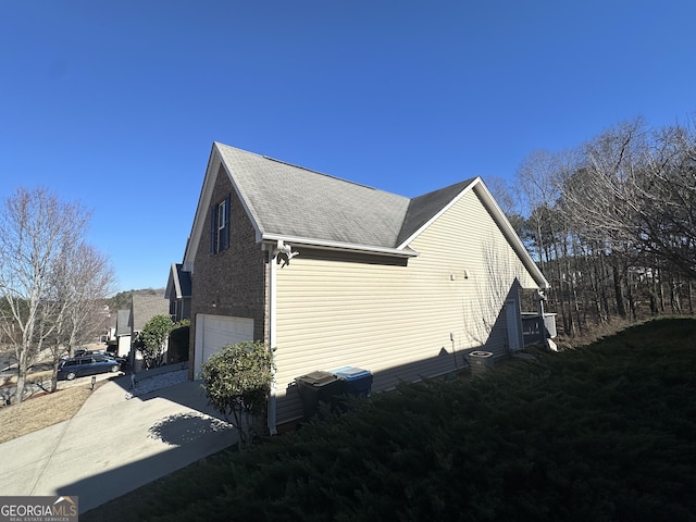 view of home's exterior with concrete driveway, brick siding, an attached garage, and roof with shingles