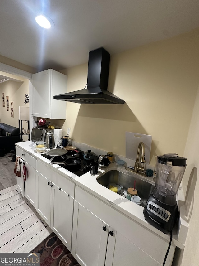 kitchen with wood finish floors, light countertops, black cooktop, white cabinets, and wall chimney range hood