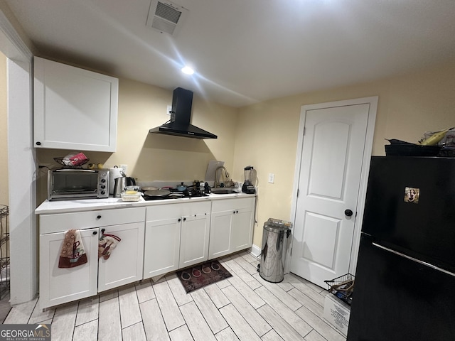 kitchen featuring visible vents, white cabinets, wall chimney range hood, black appliances, and a sink