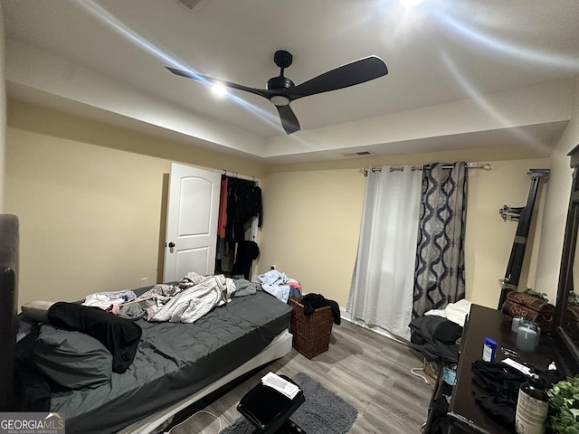 bedroom with light wood finished floors, a barn door, visible vents, a ceiling fan, and a tray ceiling