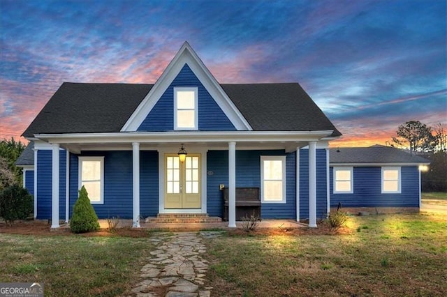 view of front facade with covered porch, french doors, and a front lawn