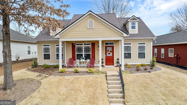 view of front facade with a porch, a shingled roof, and a front lawn