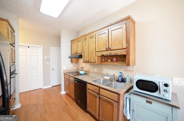 kitchen featuring tasteful backsplash, light wood-style flooring, under cabinet range hood, black appliances, and a sink