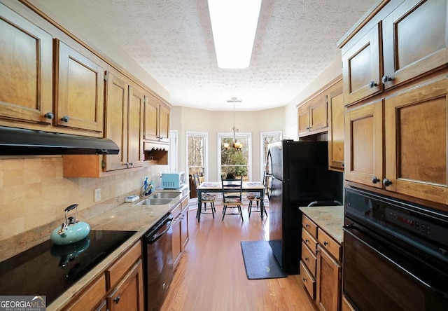 kitchen featuring light wood-style floors, backsplash, under cabinet range hood, black appliances, and a sink