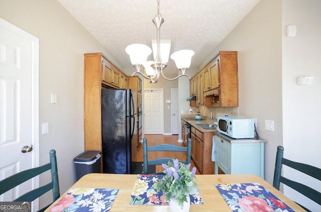 kitchen featuring a textured ceiling, white microwave, light countertops, freestanding refrigerator, and an inviting chandelier