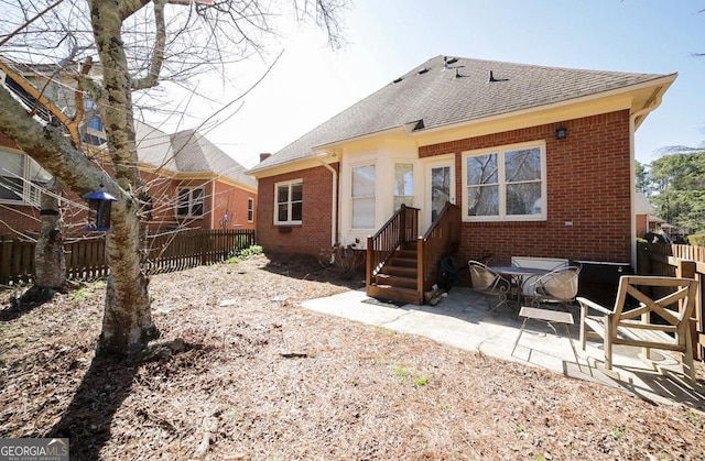 rear view of property featuring a patio, brick siding, a shingled roof, and fence