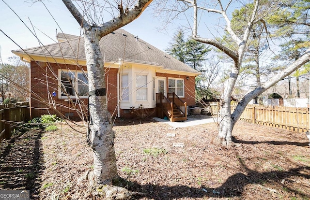 rear view of house with roof with shingles, fence, and brick siding