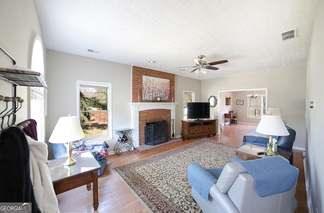 living room with a textured ceiling, ceiling fan with notable chandelier, a fireplace, wood finished floors, and visible vents