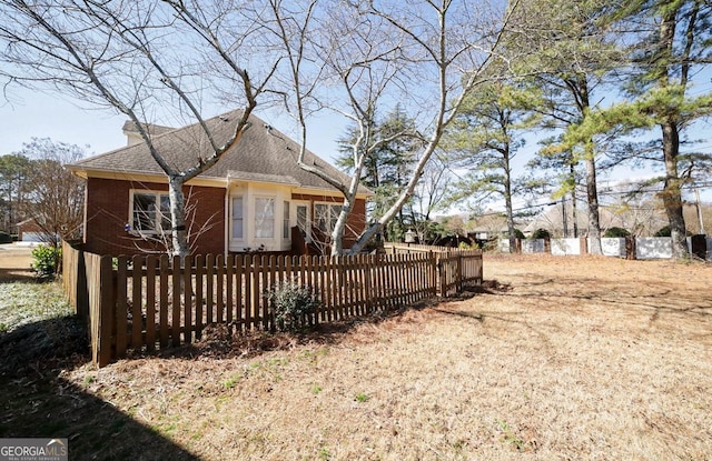 view of front of property with a fenced front yard, brick siding, and roof with shingles