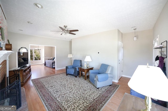 living area featuring a fireplace, a textured ceiling, baseboards, and wood finished floors