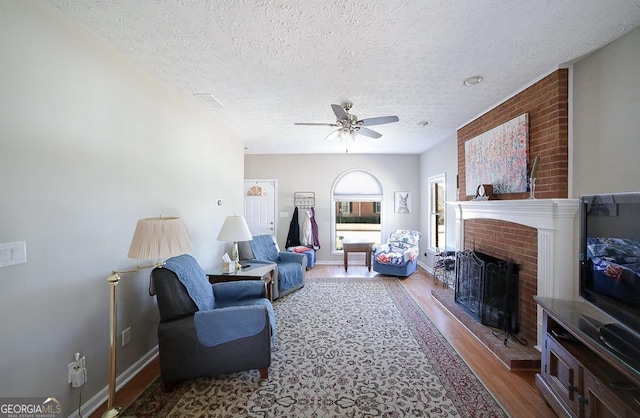 living area featuring a ceiling fan, a fireplace, a textured ceiling, and wood finished floors