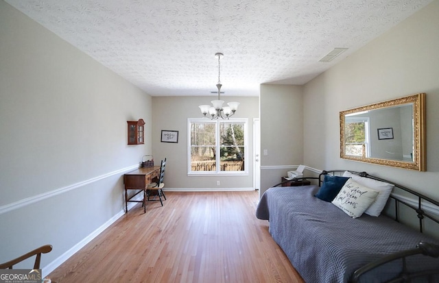 bedroom featuring baseboards, visible vents, wood finished floors, a textured ceiling, and a chandelier