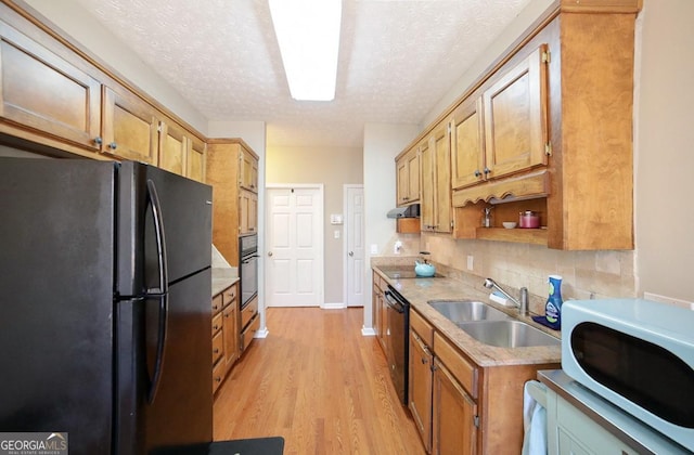 kitchen featuring a sink, light countertops, decorative backsplash, black appliances, and light wood finished floors