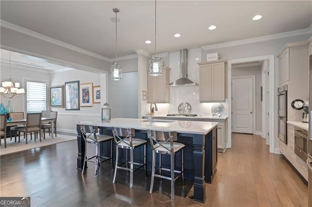 kitchen featuring wall chimney exhaust hood, a breakfast bar area, light countertops, crown molding, and a sink