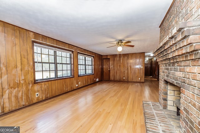 unfurnished living room featuring a ceiling fan, a brick fireplace, wood walls, and wood finished floors