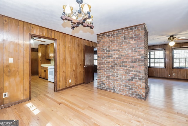 unfurnished dining area featuring light wood-type flooring, wood walls, and ceiling fan with notable chandelier