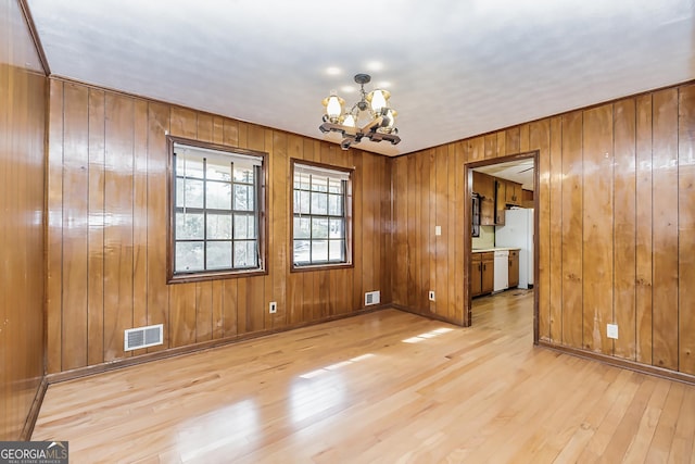 unfurnished dining area with light wood-type flooring, visible vents, baseboards, and an inviting chandelier