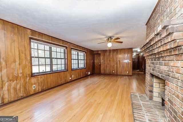 unfurnished living room featuring a ceiling fan, wood finished floors, and wooden walls