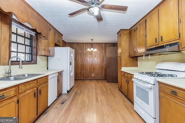 kitchen with white appliances, under cabinet range hood, brown cabinetry, and a sink