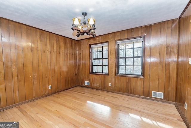 unfurnished dining area with wood-type flooring, an inviting chandelier, wooden walls, and visible vents