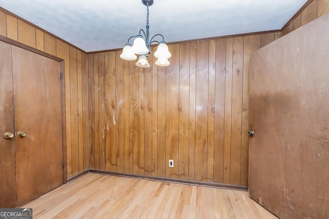 empty room with wooden walls, a notable chandelier, crown molding, and wood finished floors