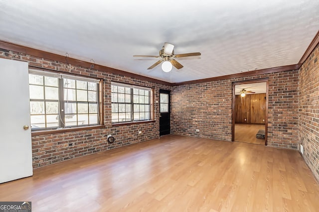 unfurnished living room featuring a ceiling fan, brick wall, and wood finished floors