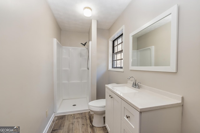 bathroom with baseboards, toilet, wood finished floors, walk in shower, and vanity