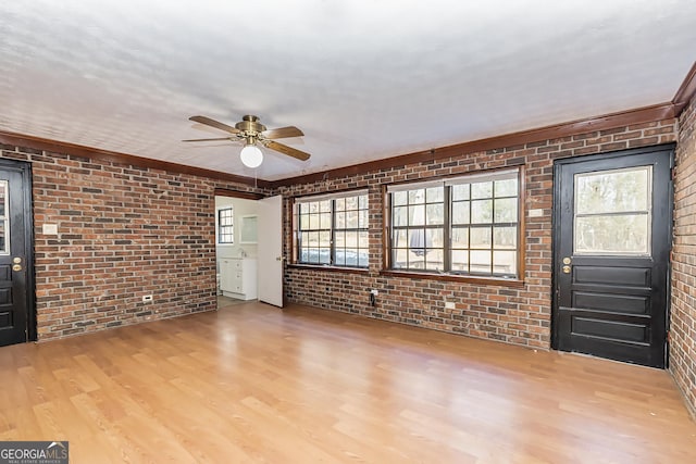 interior space with brick wall, wood finished floors, ceiling fan, and plenty of natural light