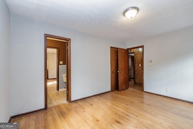 unfurnished bedroom with light wood-style floors, ensuite bath, and baseboards