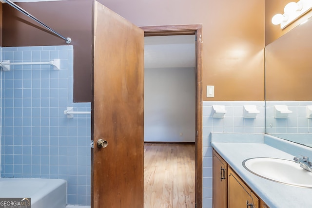 bathroom with shower / bath combination, a wainscoted wall, wood finished floors, vanity, and tile walls