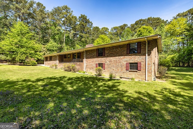rear view of property with brick siding, a lawn, and a chimney