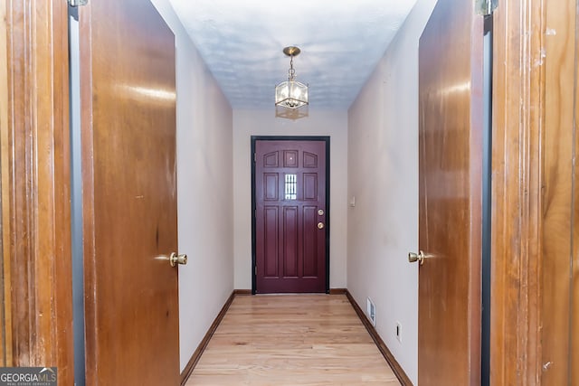 doorway to outside featuring a notable chandelier, light wood-style floors, visible vents, and baseboards