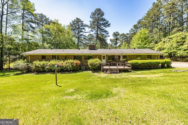 rear view of property featuring brick siding, a lawn, a chimney, and a deck