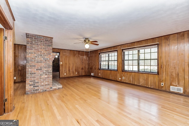 unfurnished living room with a ceiling fan, wooden walls, visible vents, and wood finished floors