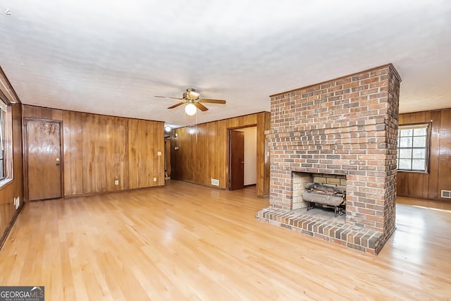 unfurnished living room with light wood-style floors, a wood stove, wood walls, and a ceiling fan