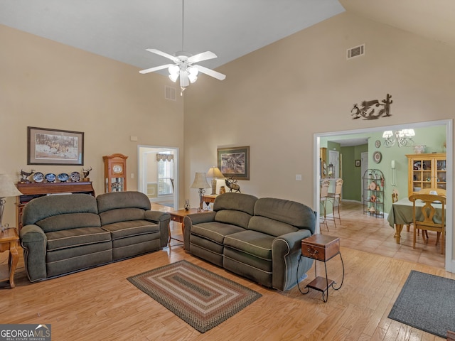 living area with light wood-type flooring, high vaulted ceiling, visible vents, and ceiling fan with notable chandelier