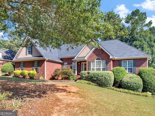 view of front of house with a front yard, roof with shingles, and brick siding