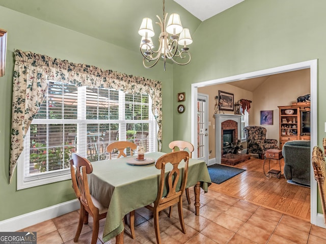 dining area with a fireplace, light tile patterned floors, lofted ceiling, a chandelier, and baseboards