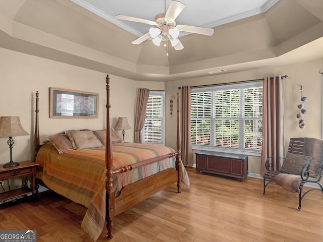 bedroom with a tray ceiling, light wood finished floors, visible vents, a ceiling fan, and baseboards