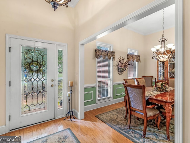 entryway featuring ornamental molding, a wainscoted wall, an inviting chandelier, and hardwood / wood-style flooring