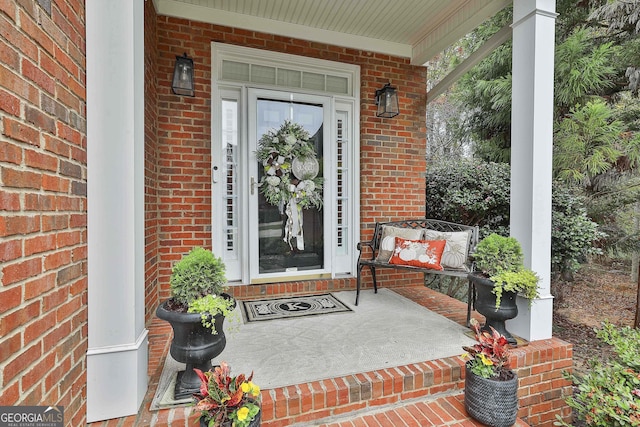 doorway to property with a porch and brick siding