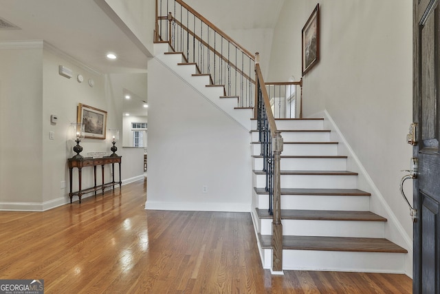 stairs featuring a high ceiling, wood finished floors, visible vents, and baseboards