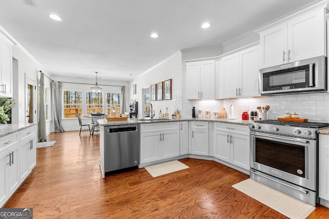 kitchen with stainless steel appliances, a peninsula, white cabinetry, and decorative backsplash